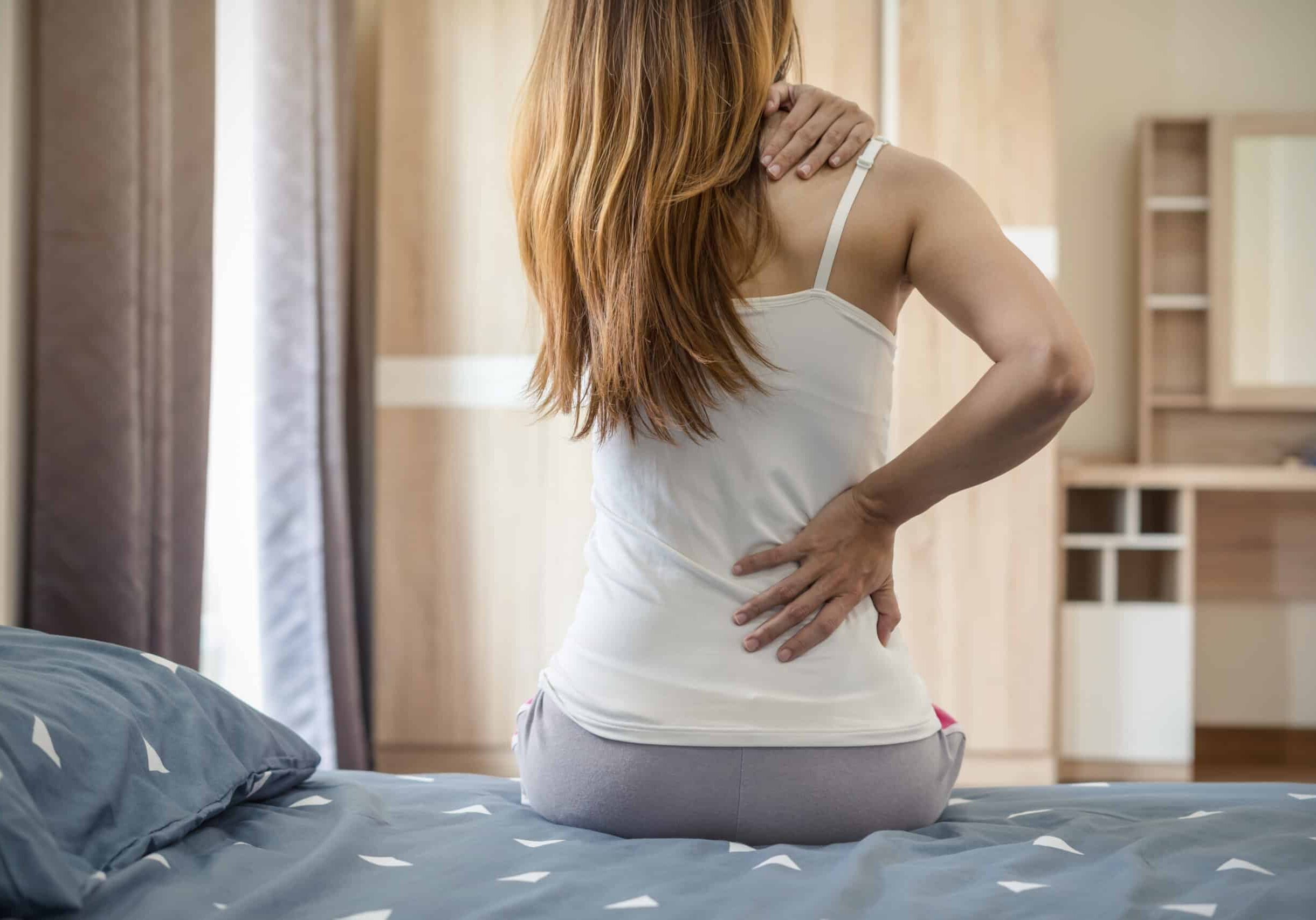Woman suffering from back ache on the bed Woman suffering from back ache on the bed, healthcare and problem concept